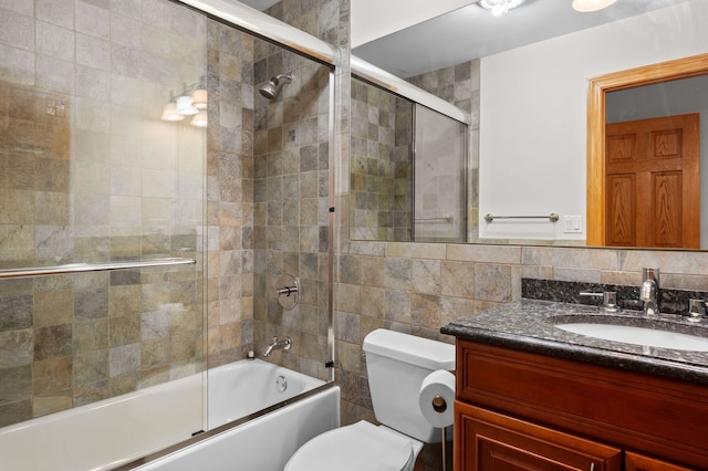 bathroom with toilet, bath / shower combo with glass door, tile walls, and vanity