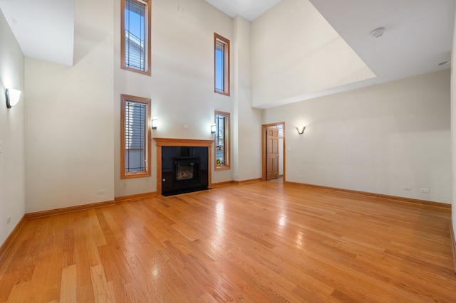 unfurnished living room featuring a tiled fireplace, a high ceiling, light wood-type flooring, and baseboards