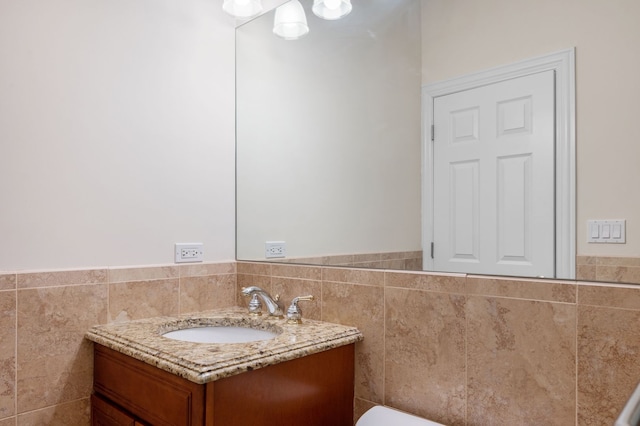 half bath with wainscoting, vanity, and tile walls