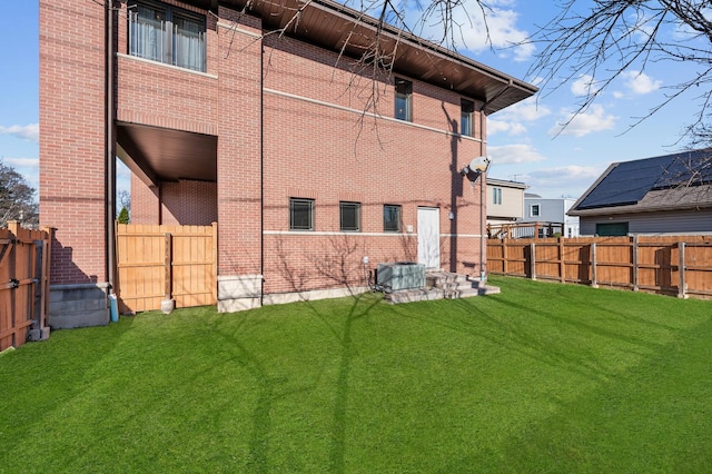 back of property featuring central AC, brick siding, a yard, and a fenced backyard