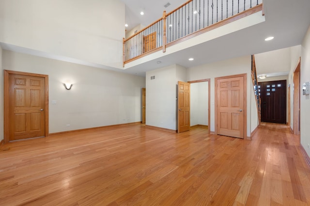 unfurnished living room featuring recessed lighting, a high ceiling, visible vents, baseboards, and light wood finished floors