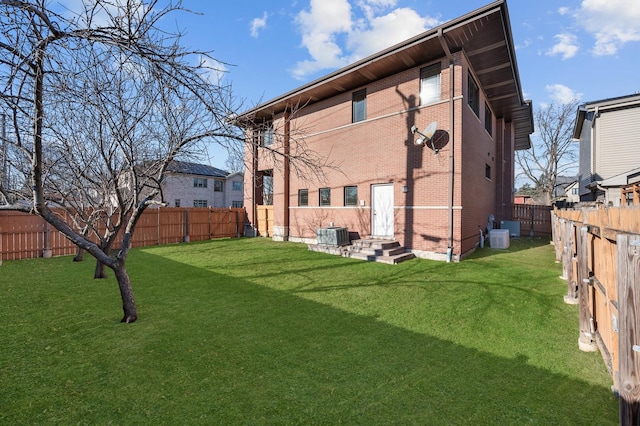 rear view of house featuring brick siding, a lawn, central AC unit, and a fenced backyard