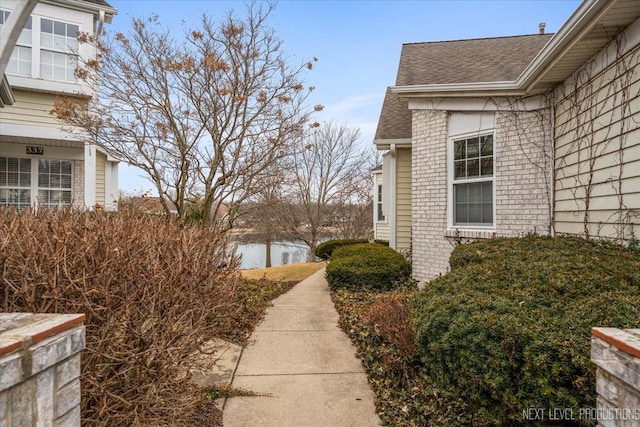 view of home's exterior featuring a water view, roof with shingles, and brick siding