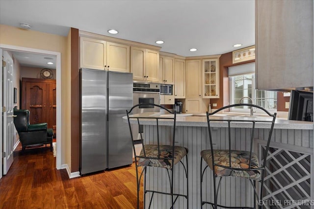 kitchen featuring a peninsula, a breakfast bar, appliances with stainless steel finishes, dark wood finished floors, and glass insert cabinets