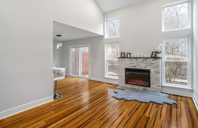 unfurnished living room featuring a high ceiling, a fireplace, wood finished floors, and baseboards