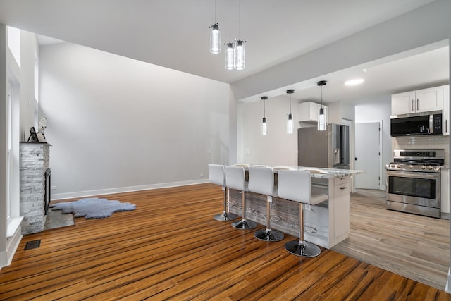 kitchen featuring tasteful backsplash, a breakfast bar area, stainless steel appliances, light wood-style floors, and a fireplace