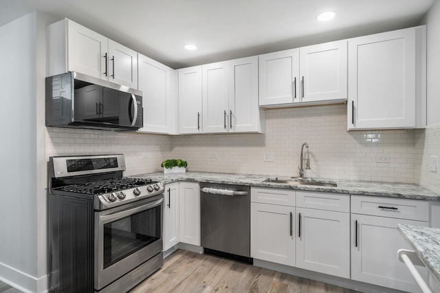 kitchen with light stone countertops, stainless steel appliances, light wood-type flooring, white cabinetry, and a sink