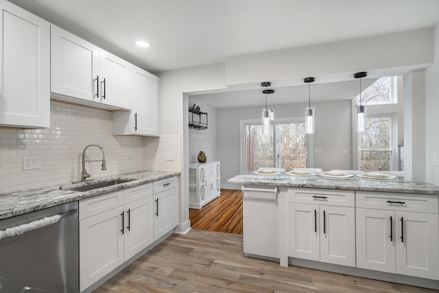 kitchen with light wood-style flooring, stainless steel dishwasher, white cabinetry, pendant lighting, and a sink