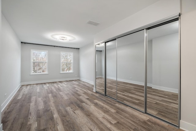 unfurnished bedroom with a closet, wood finished floors, visible vents, and baseboards