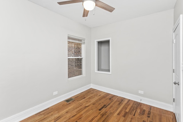 spare room with a ceiling fan, wood-type flooring, visible vents, and baseboards