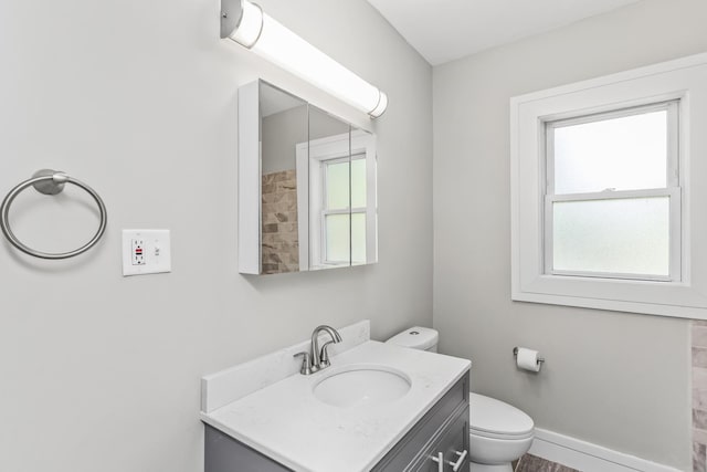 bathroom with toilet, plenty of natural light, baseboards, and vanity