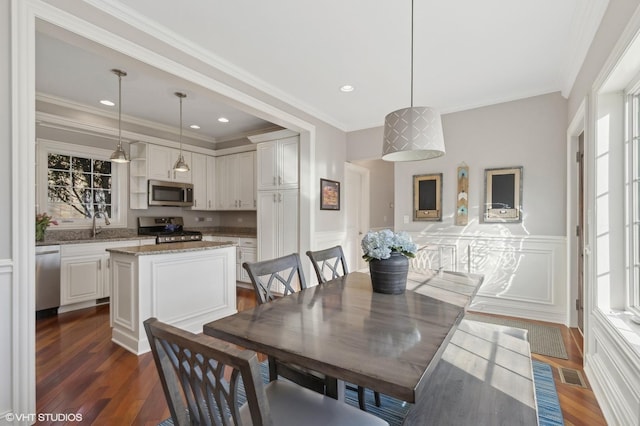 dining room featuring dark wood-style flooring, a healthy amount of sunlight, crown molding, and a wainscoted wall