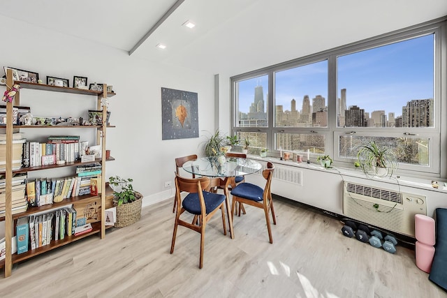 dining room featuring baseboards, beamed ceiling, a view of city, light wood-style floors, and a wall mounted AC