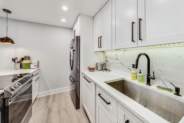 kitchen featuring light wood finished floors, white cabinets, a sink, stainless steel appliances, and backsplash