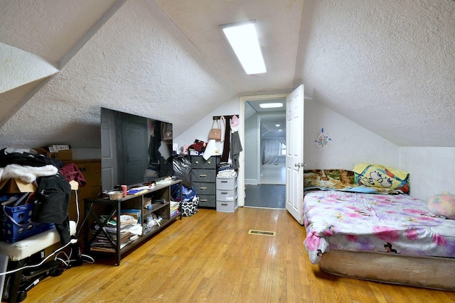 bedroom with vaulted ceiling, a textured ceiling, and wood finished floors