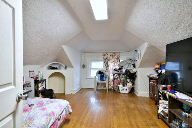 bedroom with wood-type flooring, baseboards, vaulted ceiling, and a textured ceiling