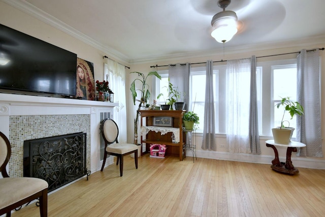 living area with hardwood / wood-style floors, ornamental molding, ceiling fan, a tile fireplace, and baseboards