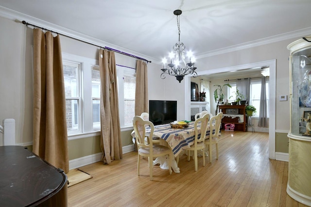 dining area featuring light wood finished floors, baseboards, crown molding, a fireplace, and a chandelier