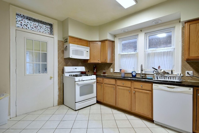 kitchen featuring light tile patterned floors, dark countertops, backsplash, a sink, and white appliances