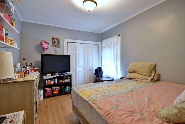 bedroom with light wood-style floors, crown molding, and a closet