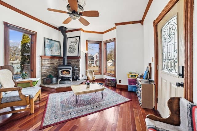 living area featuring crown molding, wood-type flooring, a wood stove, ceiling fan, and baseboards