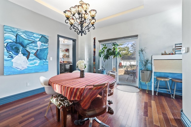 dining space with an inviting chandelier, baseboards, a raised ceiling, and wood finished floors