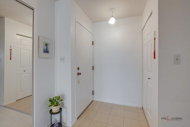 entryway with a textured ceiling, baseboards, and light tile patterned floors