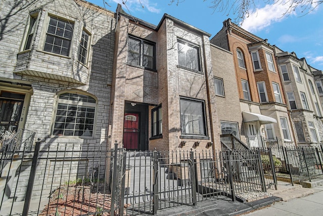 townhome / multi-family property featuring a fenced front yard and brick siding