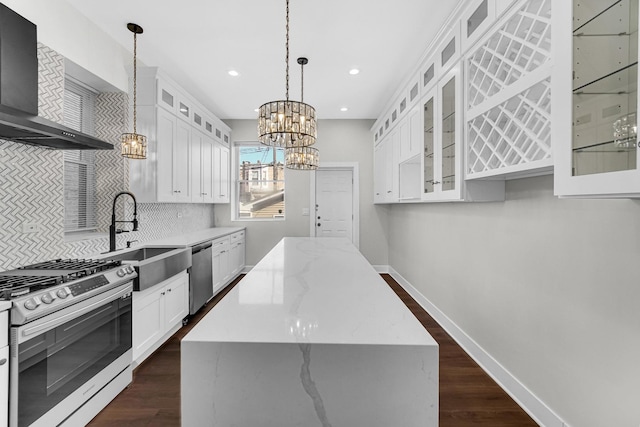 kitchen with a notable chandelier, stainless steel appliances, a kitchen island, a sink, and wall chimney range hood