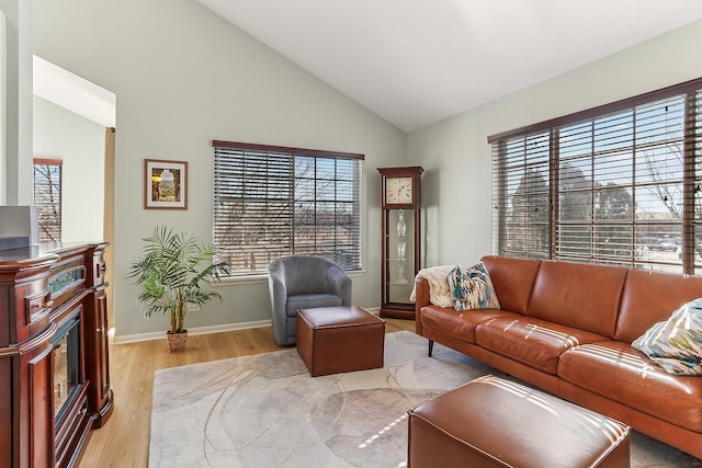 living room with light wood-style flooring, baseboards, vaulted ceiling, and a glass covered fireplace