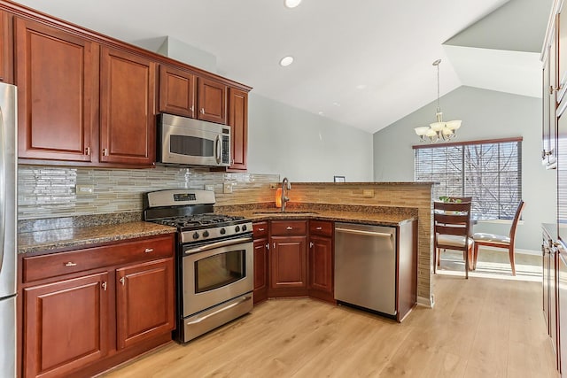 kitchen with a peninsula, a sink, light wood-style floors, vaulted ceiling, and appliances with stainless steel finishes