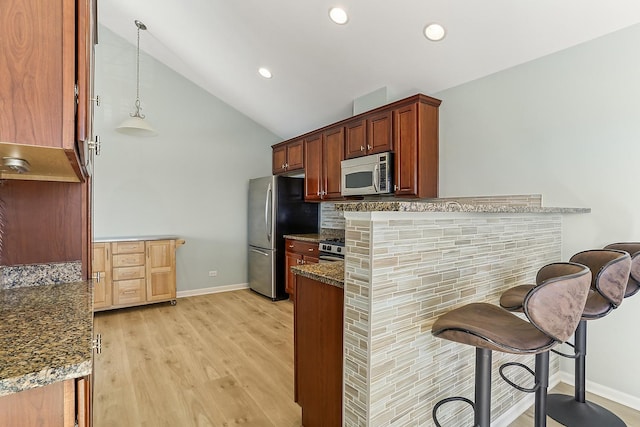 kitchen featuring tasteful backsplash, light wood-style flooring, vaulted ceiling, stainless steel appliances, and a kitchen bar