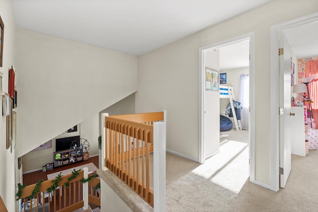 hall with an upstairs landing, baseboards, and carpet floors