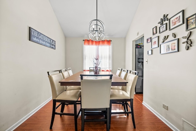 dining room featuring dark wood-type flooring, a notable chandelier, visible vents, and lofted ceiling