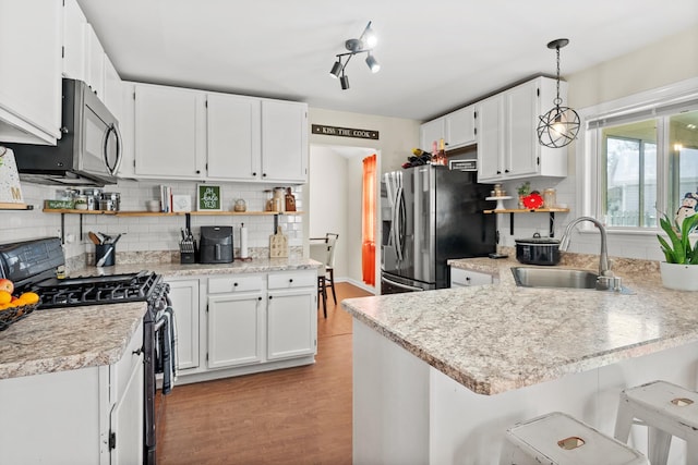 kitchen with light wood finished floors, a peninsula, a sink, stainless steel appliances, and light countertops