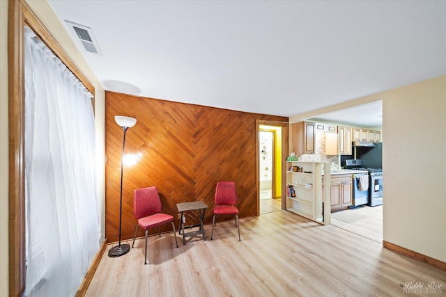 living area featuring wooden walls, light wood-type flooring, visible vents, and baseboards