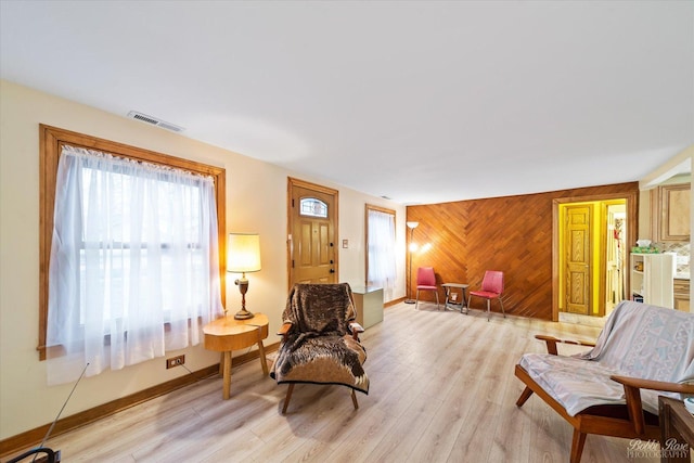 living area featuring light wood-type flooring, wood walls, baseboards, and visible vents