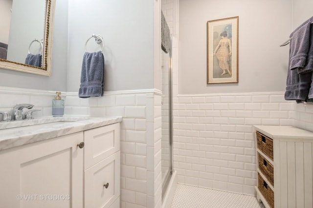 full bath with a wainscoted wall, a tile shower, tile walls, and vanity