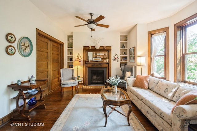 living room featuring a fireplace with raised hearth, built in shelves, plenty of natural light, and wood finished floors