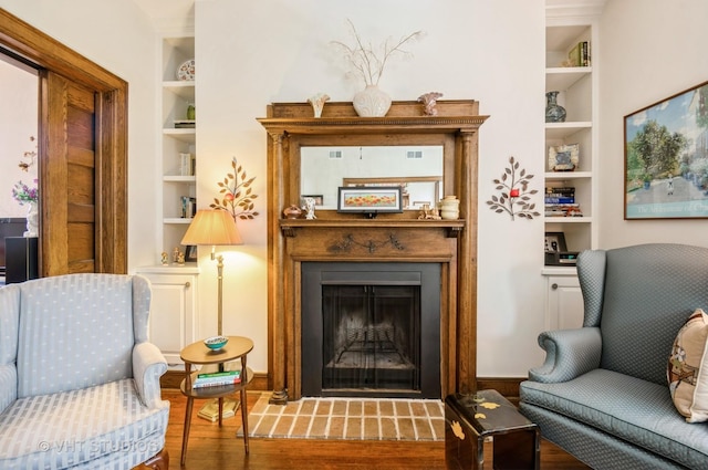 living area with built in shelves, a fireplace, and wood finished floors