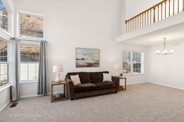 carpeted living area with a towering ceiling, an inviting chandelier, baseboards, and visible vents