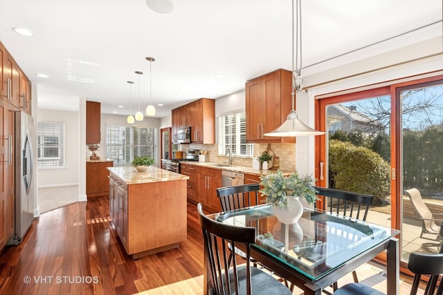 kitchen with a sink, a kitchen island, appliances with stainless steel finishes, brown cabinets, and decorative backsplash