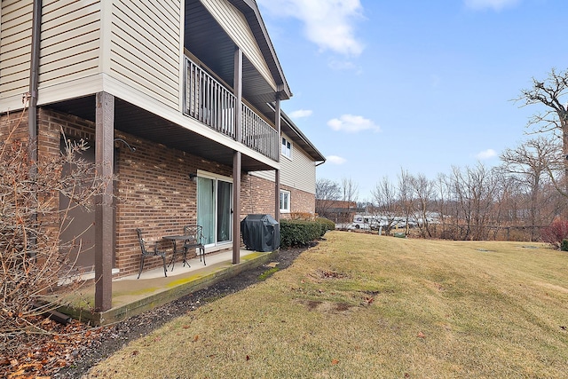 exterior space featuring a yard, brick siding, a patio area, and a balcony