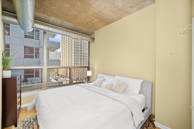 bedroom featuring floor to ceiling windows, baseboards, and wood finished floors