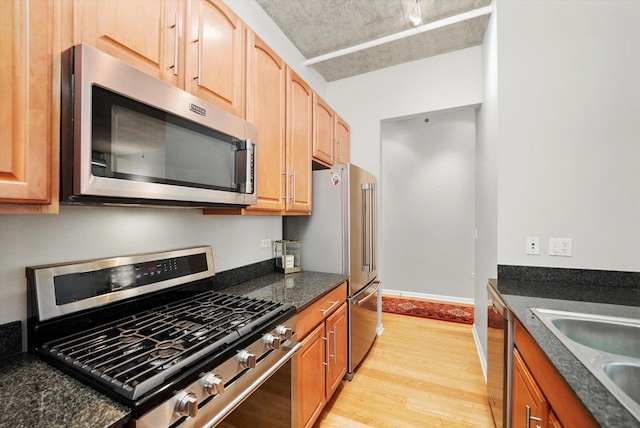 kitchen with baseboards, stainless steel appliances, light wood-type flooring, light brown cabinets, and a sink