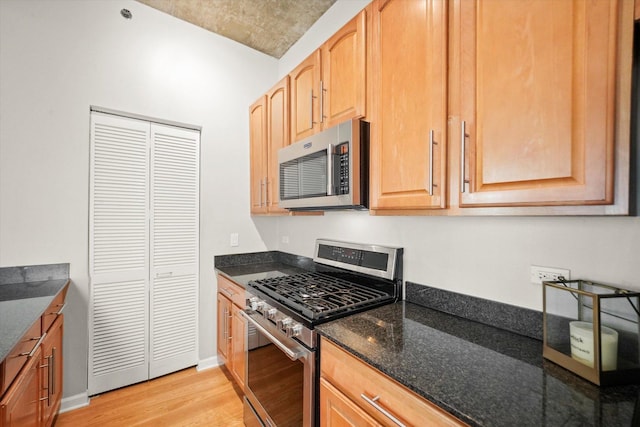 kitchen with baseboards, dark stone counters, appliances with stainless steel finishes, light wood-type flooring, and light brown cabinets