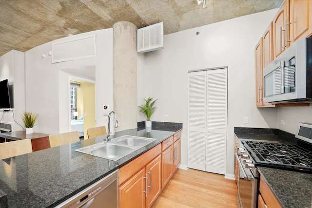 kitchen featuring stainless steel appliances, visible vents, a sink, dark stone countertops, and light wood-type flooring