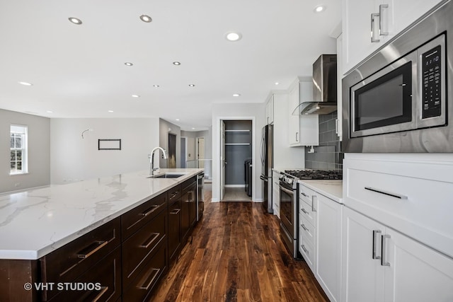 kitchen with a spacious island, backsplash, appliances with stainless steel finishes, wall chimney exhaust hood, and a sink