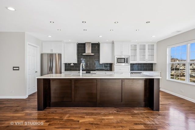 kitchen featuring a large island, white cabinetry, appliances with stainless steel finishes, wall chimney exhaust hood, and light countertops