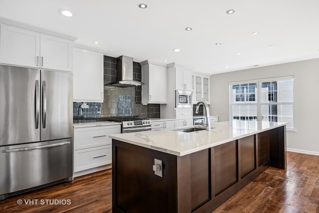 kitchen featuring an island with sink, a sink, stainless steel appliances, wall chimney exhaust hood, and backsplash